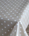 A close-up of a tablecloth with a light beige background and a repeating pattern of small white stars, draped over the table corner.