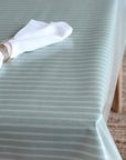 A sage green tablecloth with thin white pinstripes draped over a table, styled with a white napkin tied with twine.