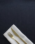 Gold fork and knife on a white napkin against a dark blue tablecloth