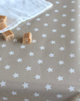 A close-up of a beige oilcloth printed with a repeating pattern of small white stars, with a folded white cloth and a few caramel candy pieces placed on top.