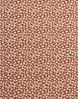 A close-up of a terracotta orange fabric with a dense, small-scale white floral or ditsy print pattern.
