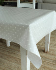 White polka dot tablecloth on a wooden table in a room with a couch and plant.