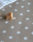 A close-up of a beige tablecloth printed with white stars, with two small pieces of light brown candy placed on it.