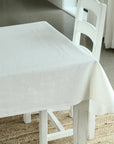 White tablecloth on a white table with chairs in a room setting.