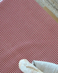 A close-up of a red and white gingham patterned tablecloth, with a white cloth and a small beige object partially visible in the lower corner.