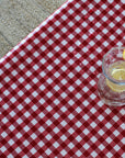 Clear glass with lemon slices on a red and white checkered tablecloth.