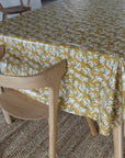 Table with a yellow floral tablecloth and a wooden chair.