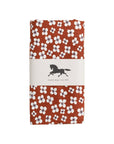 A folded oilcloth featuring a rust-orange background with a white floral pattern. It is wrapped in a white paper band with a black horse logo and the text 'Swedish design since 1846'.