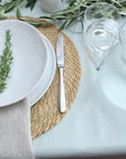 Table setting with white plates, silver knife, and glasses on a green stripe tablecloth.