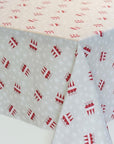 A tablecloth with a festive holiday pattern, featuring red Christmas tree silhouettes and small white snowflakes on a light gray base, draped over the corners of a table.