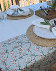 Table setting with floral tablecloth, plates, and cutlery outdoors.