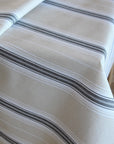A close-up of a striped tablecloth featuring horizontal stripes in dark gray, black, and white on a warm off-white background.
