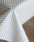 White tablecloth with a repeating gray leaf or teardrop pattern, draped over a table with a textured beige woven surface visible underneath.