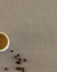 White cup of coffee and scattered coffee beans on a beige linen tablecloth