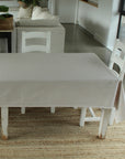 Dining table with a grey linen tablecloth in a room with a rug and chairs.