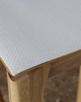 Close-up of a white textured table mat with a subtle grid pattern, shown on a light wood table.