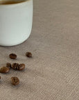 White ceramic cup and coffee beans on a textured beige linen tablecloth
