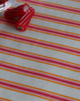 A close-up of a striped oilcloth with alternating pink, orange, and white horizontal lines, with small red cylindrical beads or clips placed near the top left on top of the fabric.