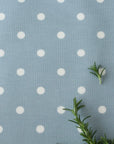 Oilcloth with white polka dots on a blue background with green leaves.