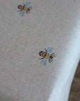 Close-up of tablecloth with embroidered bee designs on a neutral background