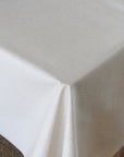 A close-up of a beige tablecloth draped over a table corner, showing its smooth texture and soft folds.