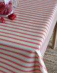 A close-up of a table covered with a tablecloth featuring thin red and pink horizontal stripes. A glass jar filled with red candy sits on the table, with a few pieces spilled.