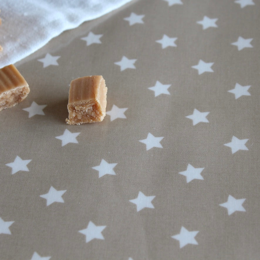 A close-up of a beige tablecloth printed with white stars, with two small pieces of light brown candy placed on it.