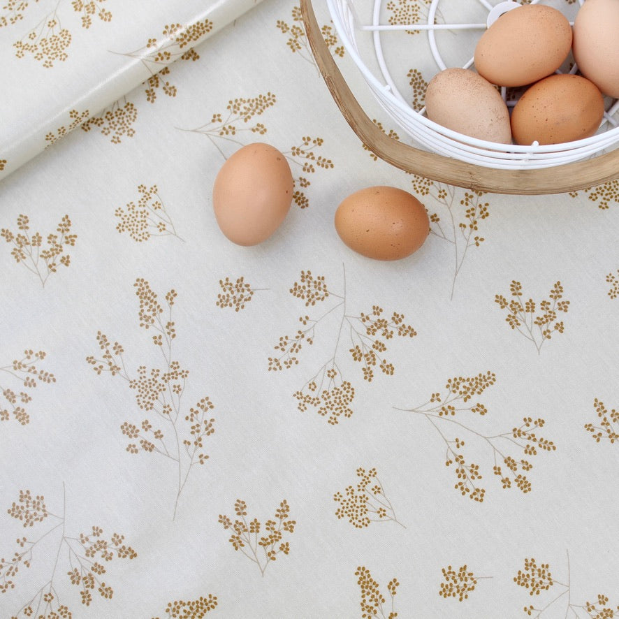Three brown eggs on a floral-patterned oilcloth with a basket of eggs in the background.