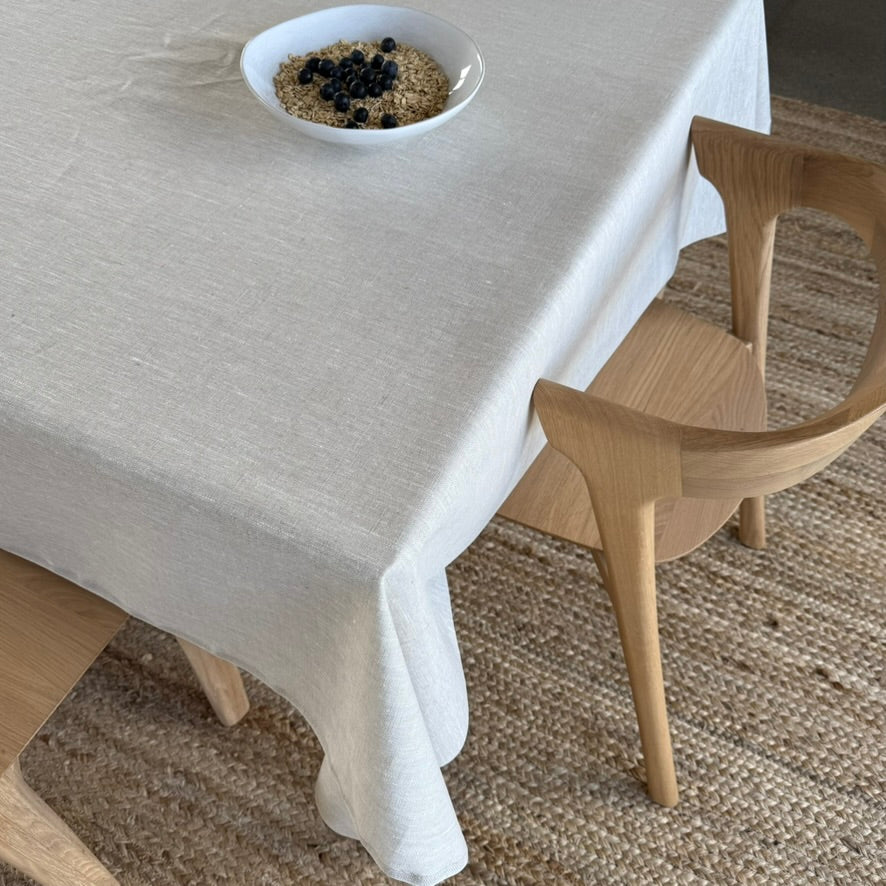 Beige tablecloth on a dining table with a bowl of food and a wooden chair.