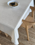 Beige tablecloth on a dining table with a bowl of food and a wooden chair.