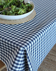 A navy and white gingham checkered tablecloth draped over a table, with a white bowl of salad on a woven placemat in the upper left.