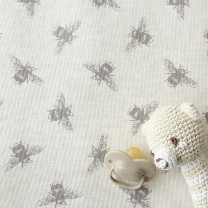 Baby pacifier and white knitted toy on an oilcloth with beige bee pattern.