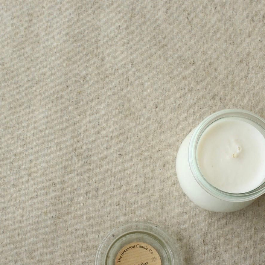 White candle in a glass jar on a beige oilcloth