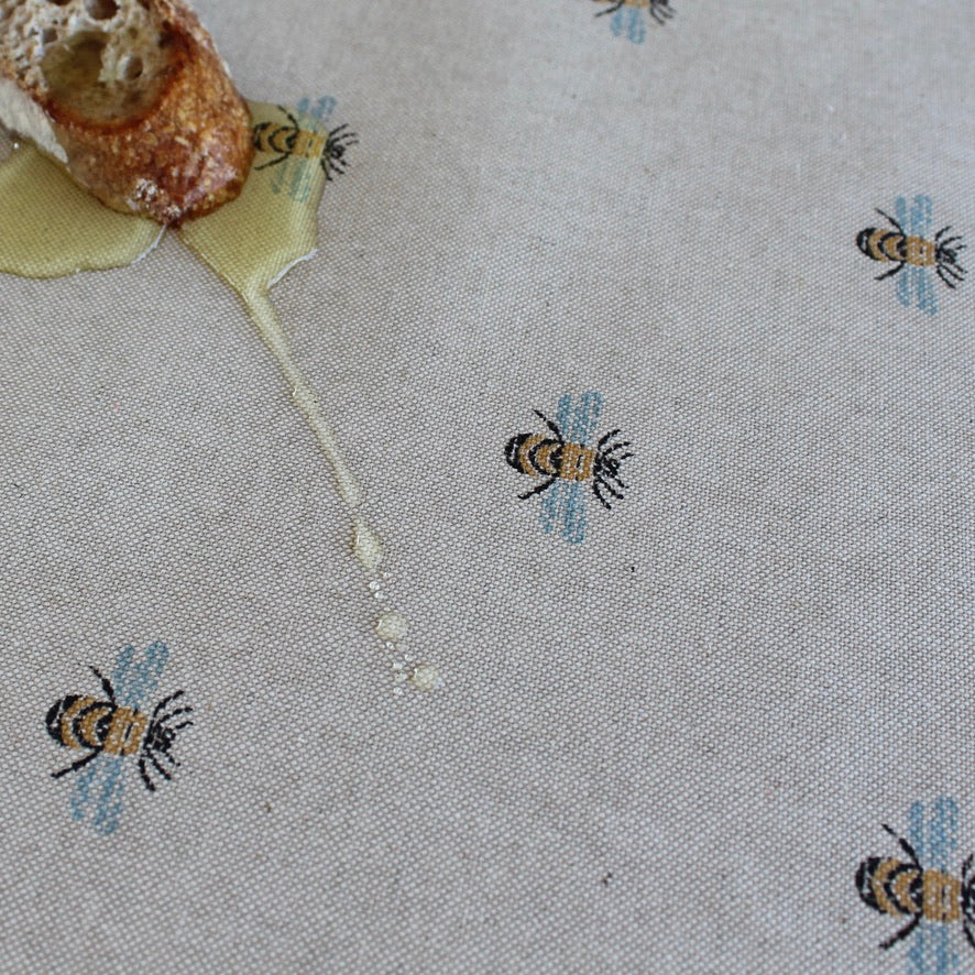 Honeycomb with honey dripping onto a tablecloth with bee patterns.