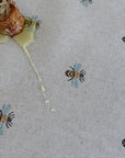 Honeycomb with honey dripping onto a tablecloth with bee patterns.