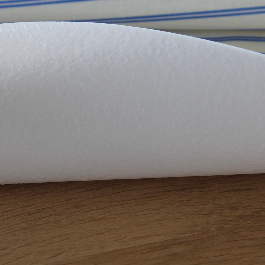 A close-up of a white textured table protector resting on a wooden surface, with a striped fabric visible in the background.
