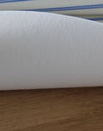 A close-up of a white textured table protector resting on a wooden surface, with a striped fabric visible in the background.