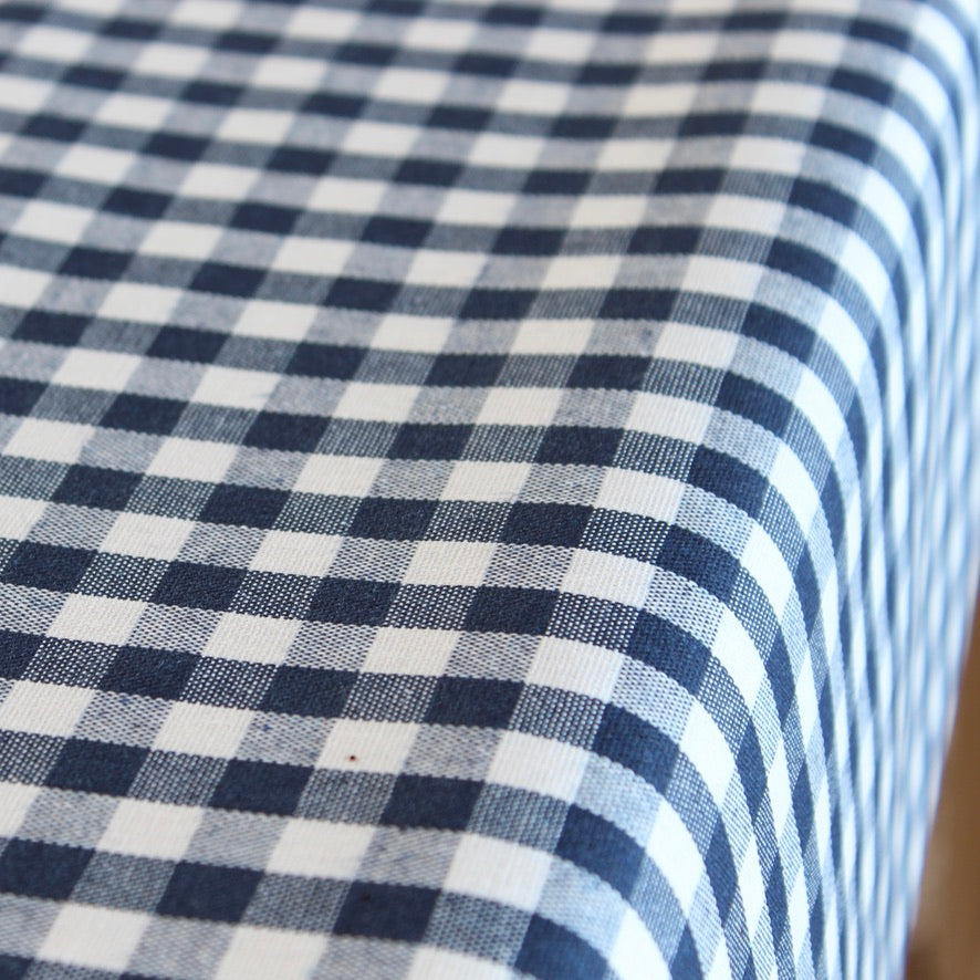 A close-up of a navy blue and white gingham checkered tablecloth draped over the corner of a table.