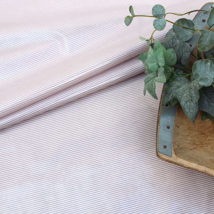Close-up of a subtle pink striped oilcloth with a plant in the corner