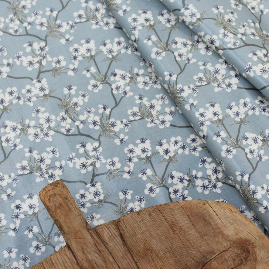 Floral patterned oilcloth with white flowers on a blue background with a wooden board