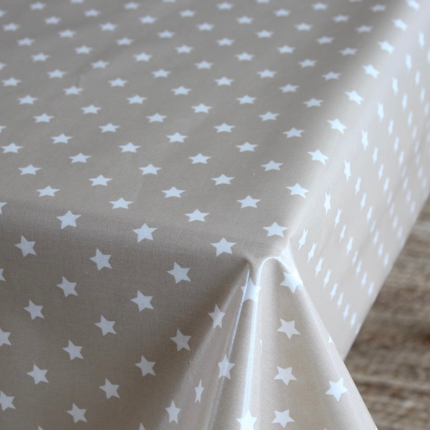 A close-up of a tablecloth with a light beige background and a repeating pattern of small white stars, draped over the table corner.