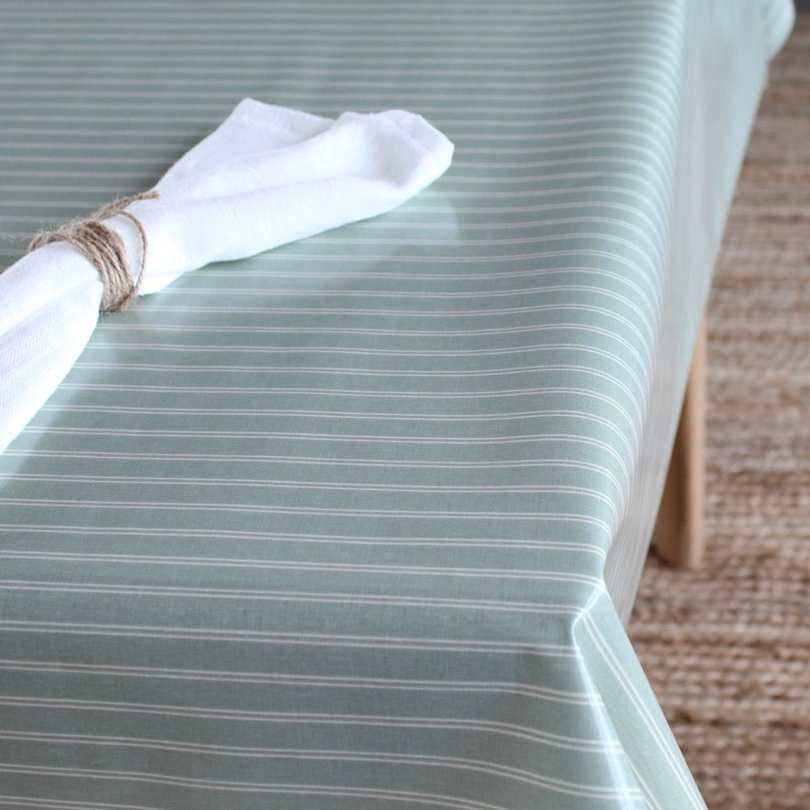 A sage green tablecloth with thin white pinstripes draped over a table, styled with a white napkin tied with twine.