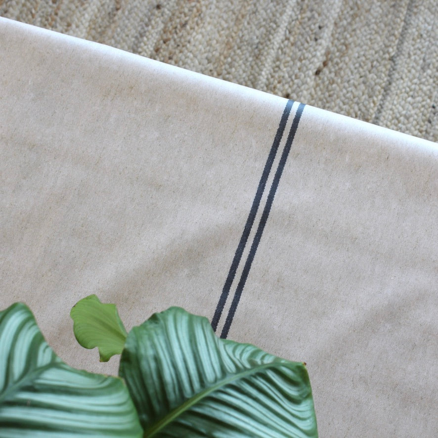 Close-up of a beige tablecloth with black stripes and green leaf.