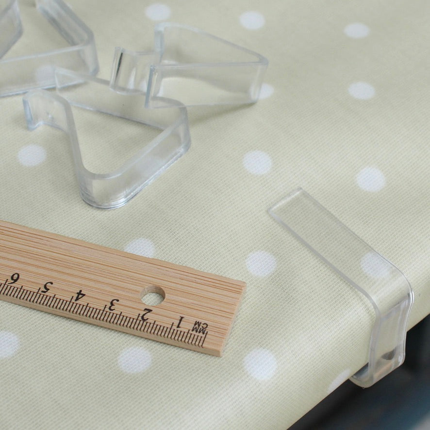 Clear plastic tablecloth clips on a polka dot fabric surface with a wooden ruler for scale.