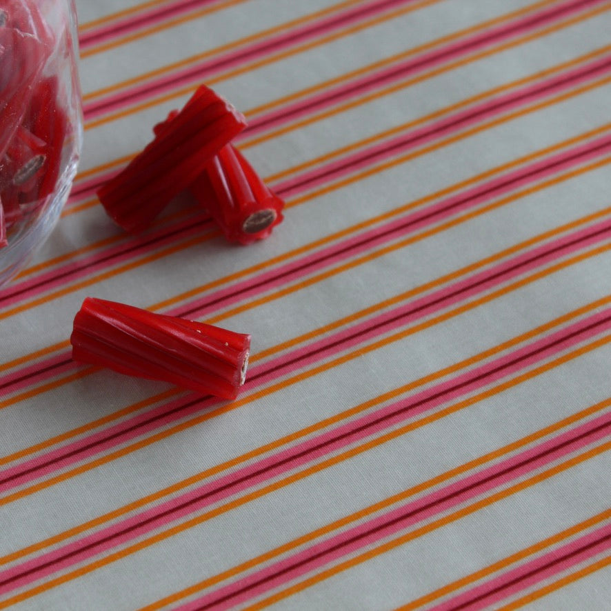 Red licorice candy pieces on a tablecloth with pink and orange diagonal stripes, with a plastic bag partially visible on the left.