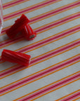 Red licorice candy pieces on a tablecloth with pink and orange diagonal stripes, with a plastic bag partially visible on the left.