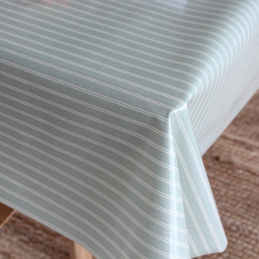 A close-up of a tablecloth with a pale sage green background and thin white vertical stripes, draped over a table corner.