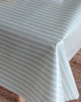 A close-up of a tablecloth with a pale sage green background and thin white vertical stripes, draped over a table corner.