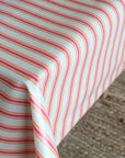 A close-up of a tablecloth with thin pink, orange, and yellow diagonal stripes, draped over the corner of a table with a textured beige rug visible underneath.