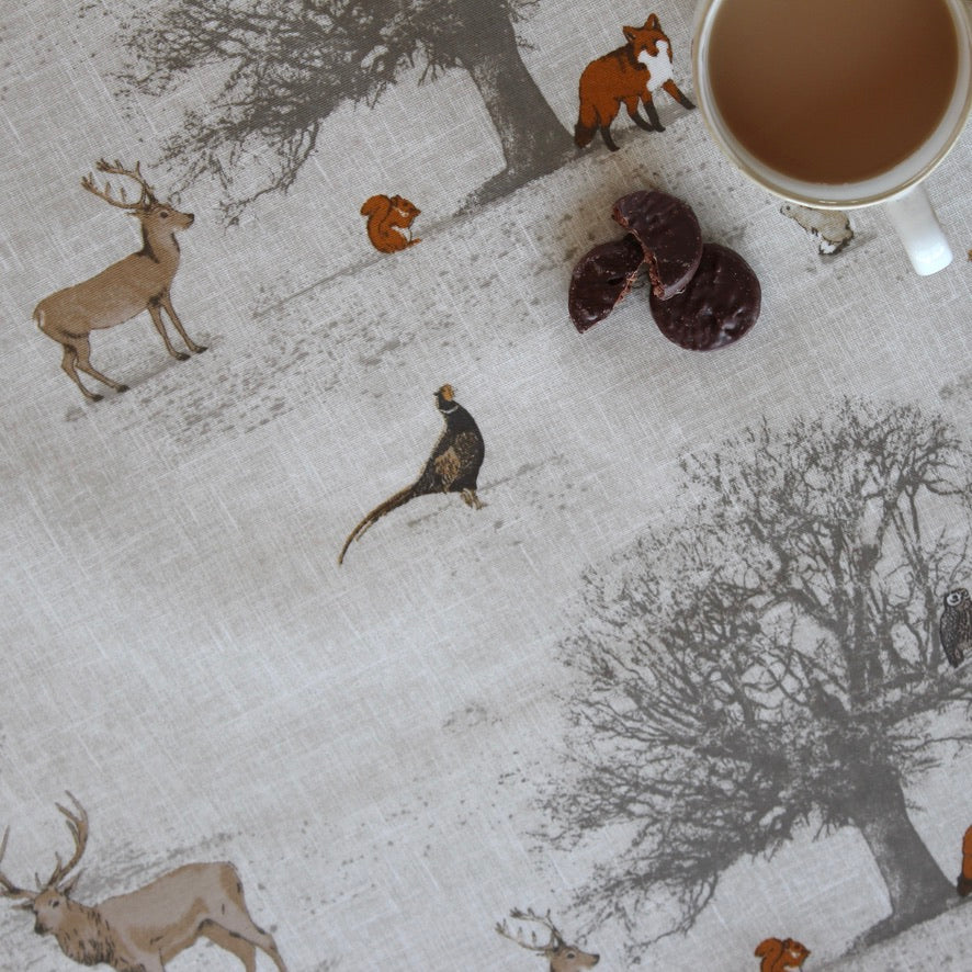 Woodland animal pattern oilcloth with deer, fox, and badger on a textured surface with a cup of coffee.